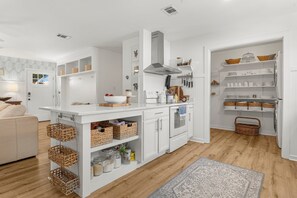 A modern kitchen with white cabinetry, a built-in oven, and a large island with baskets and jars.