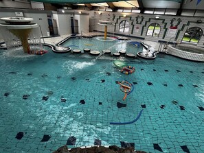An indoor swimming pool with multiple lanes, a water slide, and a diving platform.