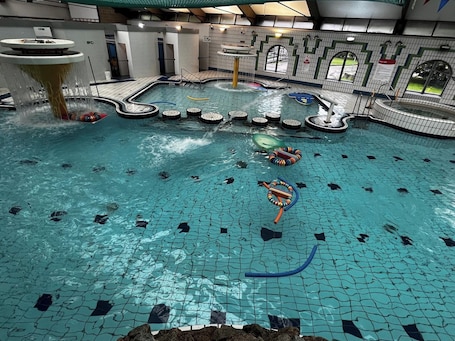 An indoor swimming pool with multiple lanes, a water slide, and a diving platform.