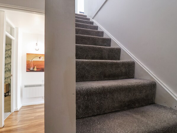 A carpeted staircase with a white handrail and a door leading to a room with a radiator and a painting.