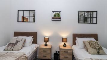 Habitación doble con dos camas, cada una con cabecera, mesitas de noche con lámparas y una obra de arte colgada en la pared.