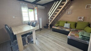 A cozy room with a wooden floor, a dining table with chairs, a sofa with cushions, and a staircase.