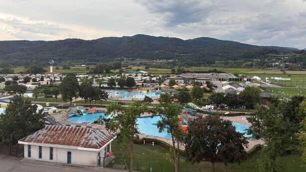 A resort with multiple swimming pools, a tennis court, and a view of surrounding hills.