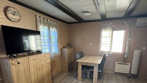 A room with a wooden cabinet, a flat-screen TV, a dining table with chairs, and a window with curtains.
