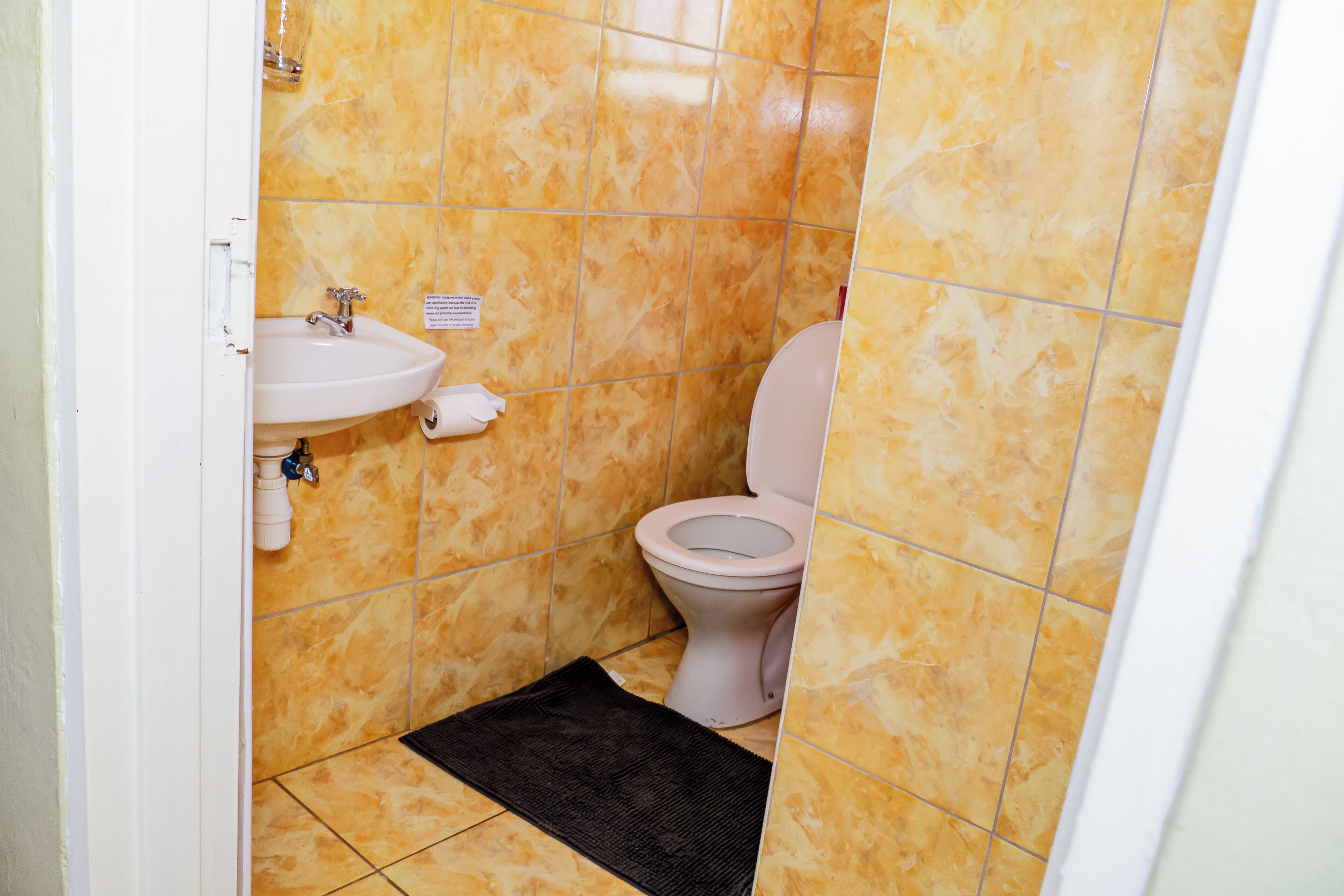 A bathroom with a sink, toilet, and a black mat on the floor.