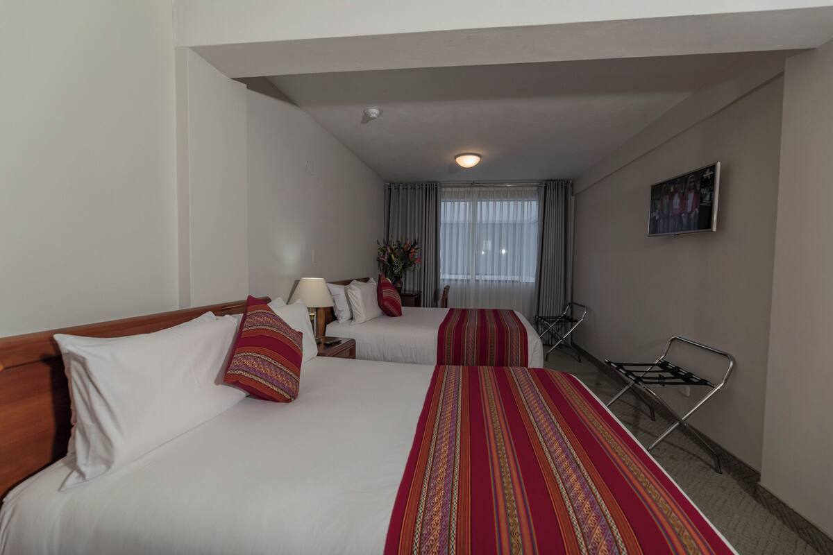 A hotel room with two beds, a desk, a chair, a lamp, and a window with curtains.