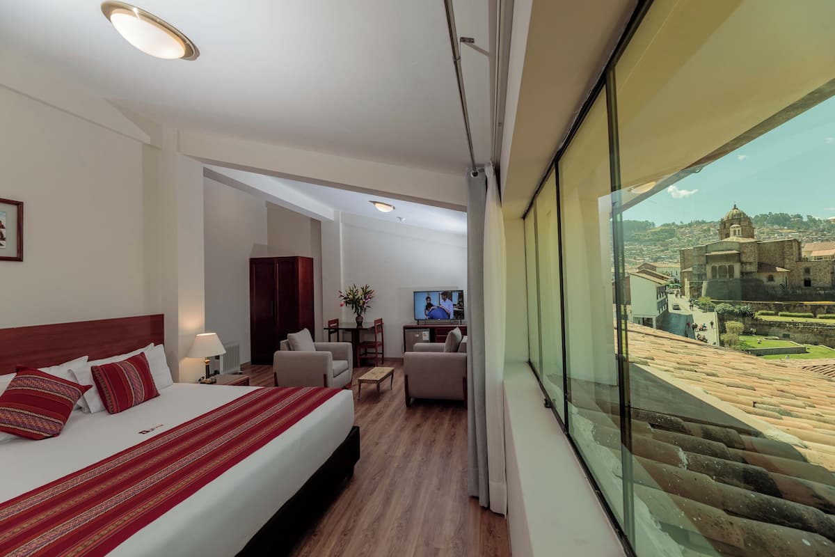 A hotel room with a large bed, a TV, a desk, and a view of a historic building.