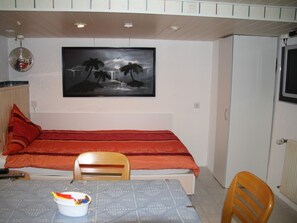 A room with a bed, a table with a bucket, a chair, a painting of a waterfall, and a disco ball. - Studio 'Jülich' with Private Terrace, Shared Garden and Wi-Fi (Weil am Rhein)