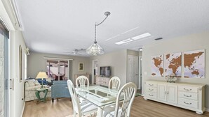 Un comedor amplio con una mesa de vidrio y sillas blancas, un ventilador de techo y un mapa mundial en la pared.