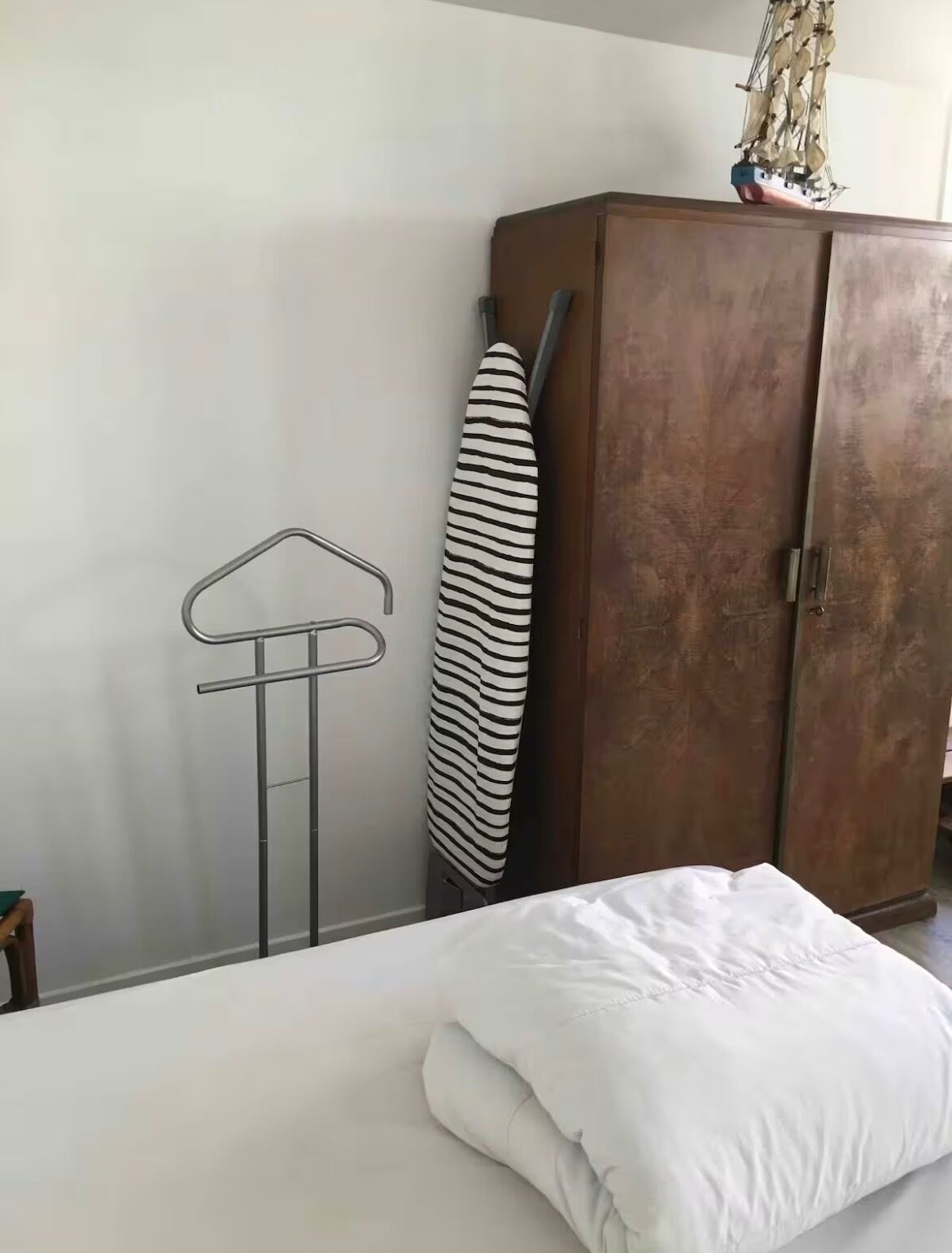A bedroom with a bed, a wardrobe, a hanging clothes rack, and a striped towel.