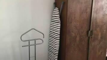 A bedroom with a bed, a wardrobe, a hanging clothes rack, and a striped towel.