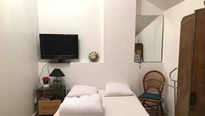 A bedroom with a bed, a TV mounted on the wall, a nightstand with a lamp, a chair, and a wardrobe. - Studio BEACH ENTRANCE and Free Parking (Ouistreham)