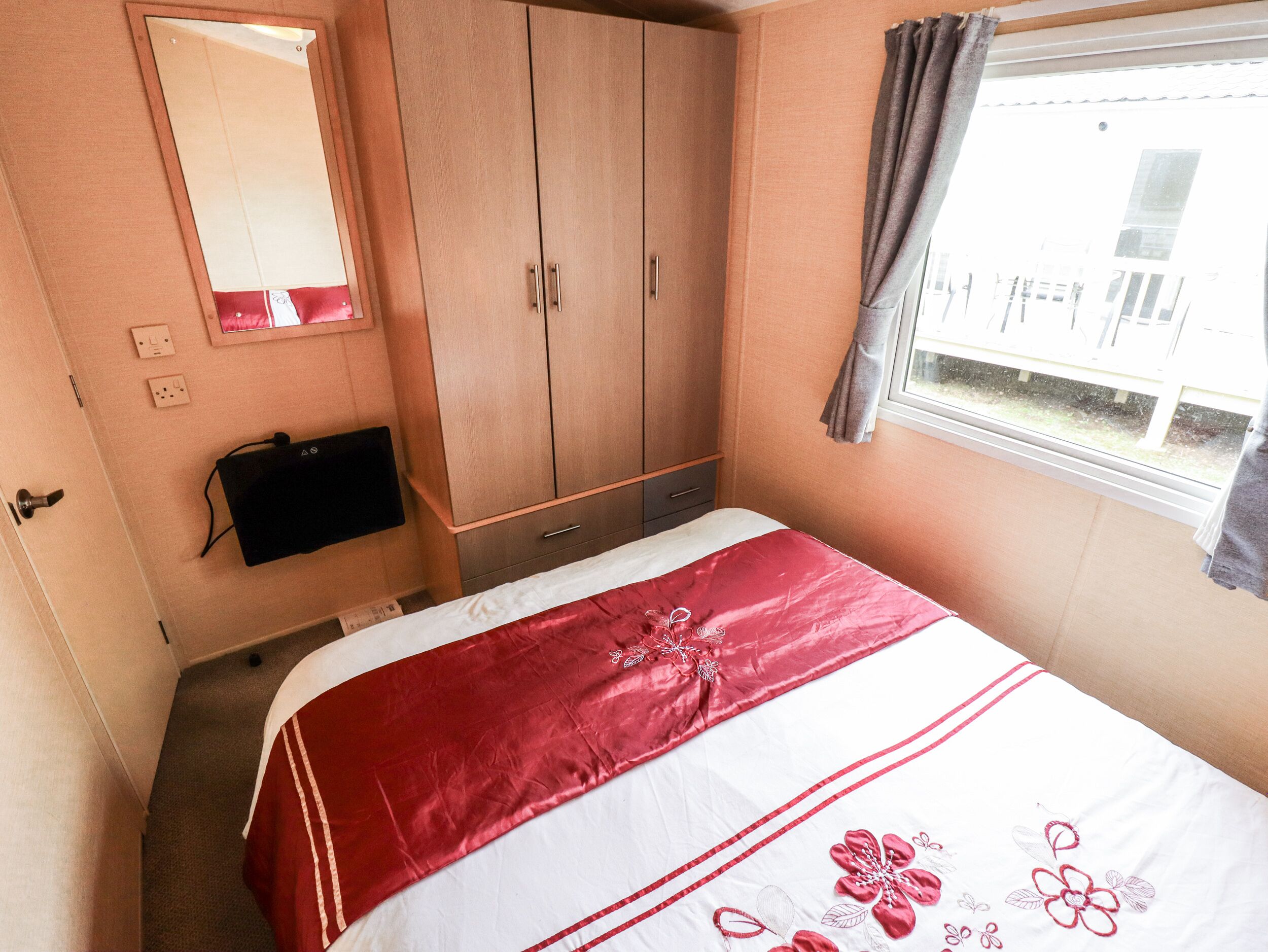 A bedroom with a bed, a wardrobe, a mirror, and a window.