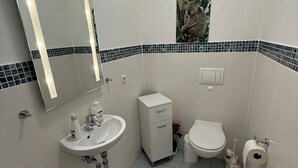 A bathroom with a white sink, toilet, and bidet, a small cabinet, and a mirror with a light strip. - MLK-Lodge: Your vacation apartment on the Mittelland Canal (Sehnde)