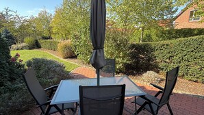 An outdoor patio with a table and chairs, surrounded by a garden and a brick pathway. - MLK-Lodge: Your vacation apartment on the Mittelland Canal (Sehnde)