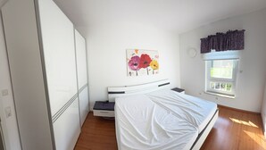 A bedroom with a bed, a nightstand, a wardrobe, a window with curtains, and a painting on the wall. - MLK-Lodge: Your vacation apartment on the Mittelland Canal (Sehnde)