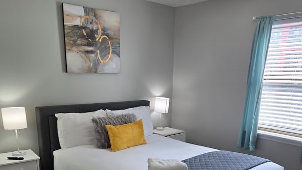 Ein ordentlich eingerichtetes Schlafzimmer mit Bett, Nachttischen, einer Lampe und einem Gemälde an der Wand.