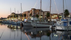 A marina with boats docked, buildings in the background, and a clear sky.