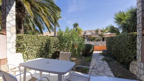 A patio with a table and chairs, surrounded by hedges and palm trees.