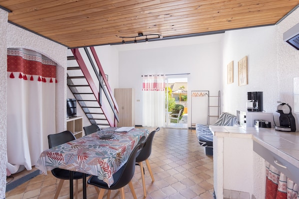 A dining area with a table, chairs, and a kitchen area with appliances.