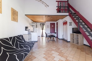 A living room with a sofa, a dining table, and a kitchen area with a coffee machine.