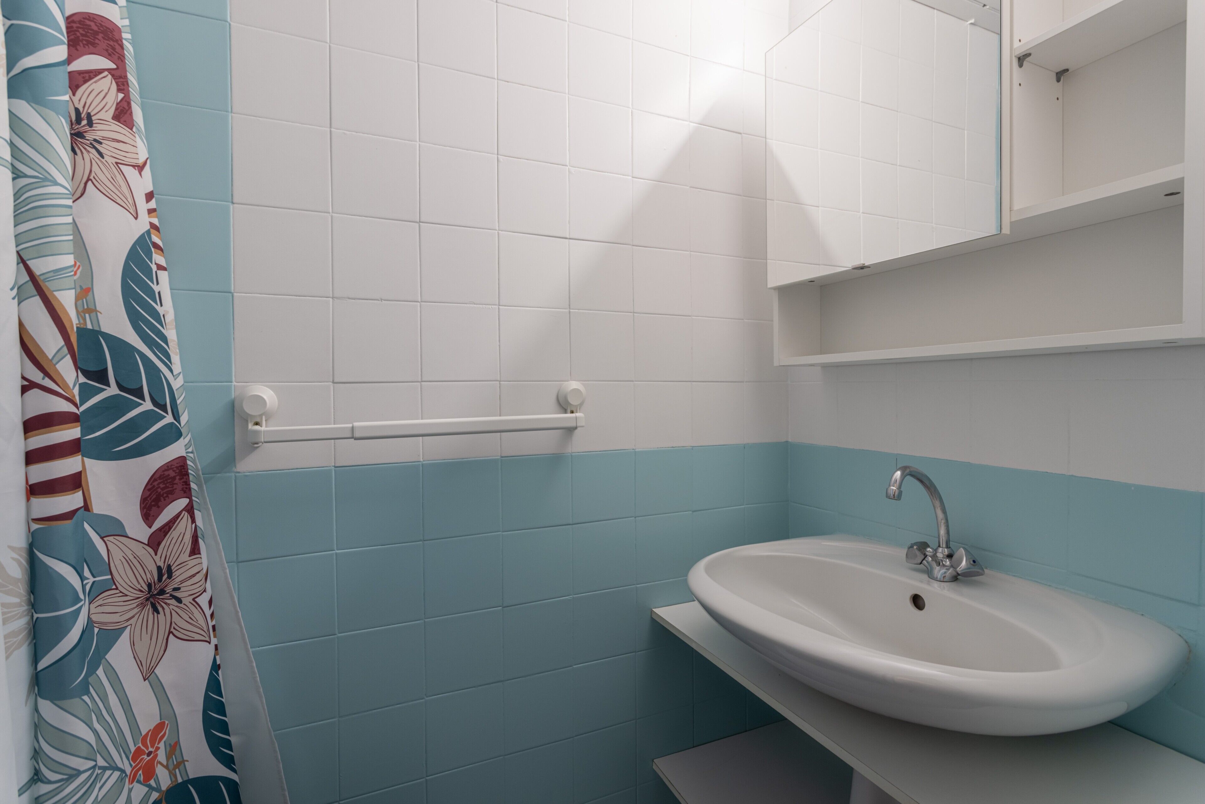 A bathroom with a white sink, a mirror, and a shower curtain with a floral pattern.