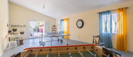 A room with a foosball table, a ping pong table, and a clock on the wall.