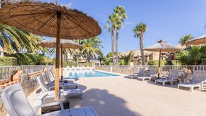 A poolside area with lounge chairs, umbrellas, and palm trees.