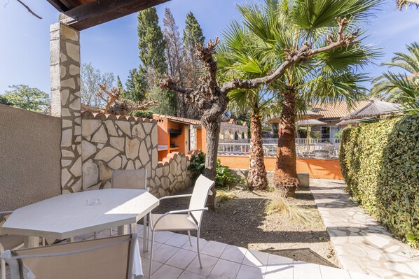 Un patio al aire libre con una mesa y sillas, rodeado de muros de piedra y palmeras.