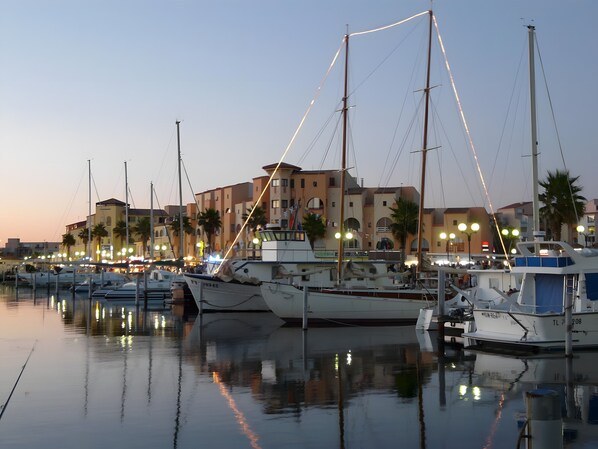 A marina with boats docked, buildings in the background, and a clear sky.