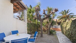 An outdoor patio with a white table and blue chairs, surrounded by a garden with palm trees and a stone pathway.