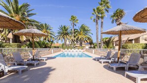 A pool area with lounge chairs and umbrellas, surrounded by palm trees and a clear sky.