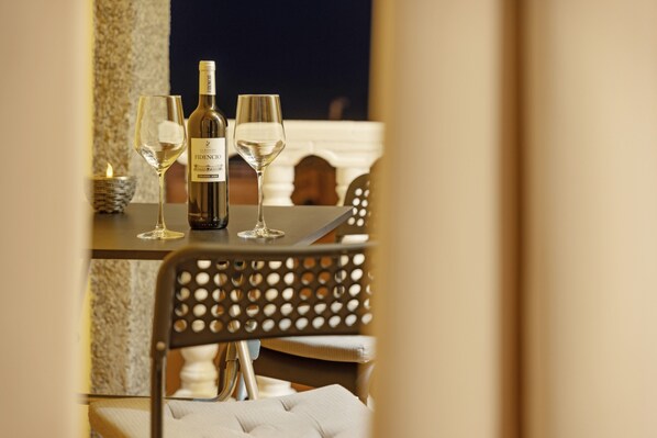 A table with a bottle of wine and two glasses, a candle, and a chair with a perforated backrest.