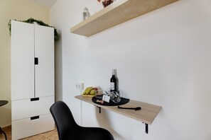 Ein modernes Zimmer mit einem weißen Kleiderschrank, einem Holzregal mit einer Flasche und Früchten sowie einem schwarzen Stuhl.