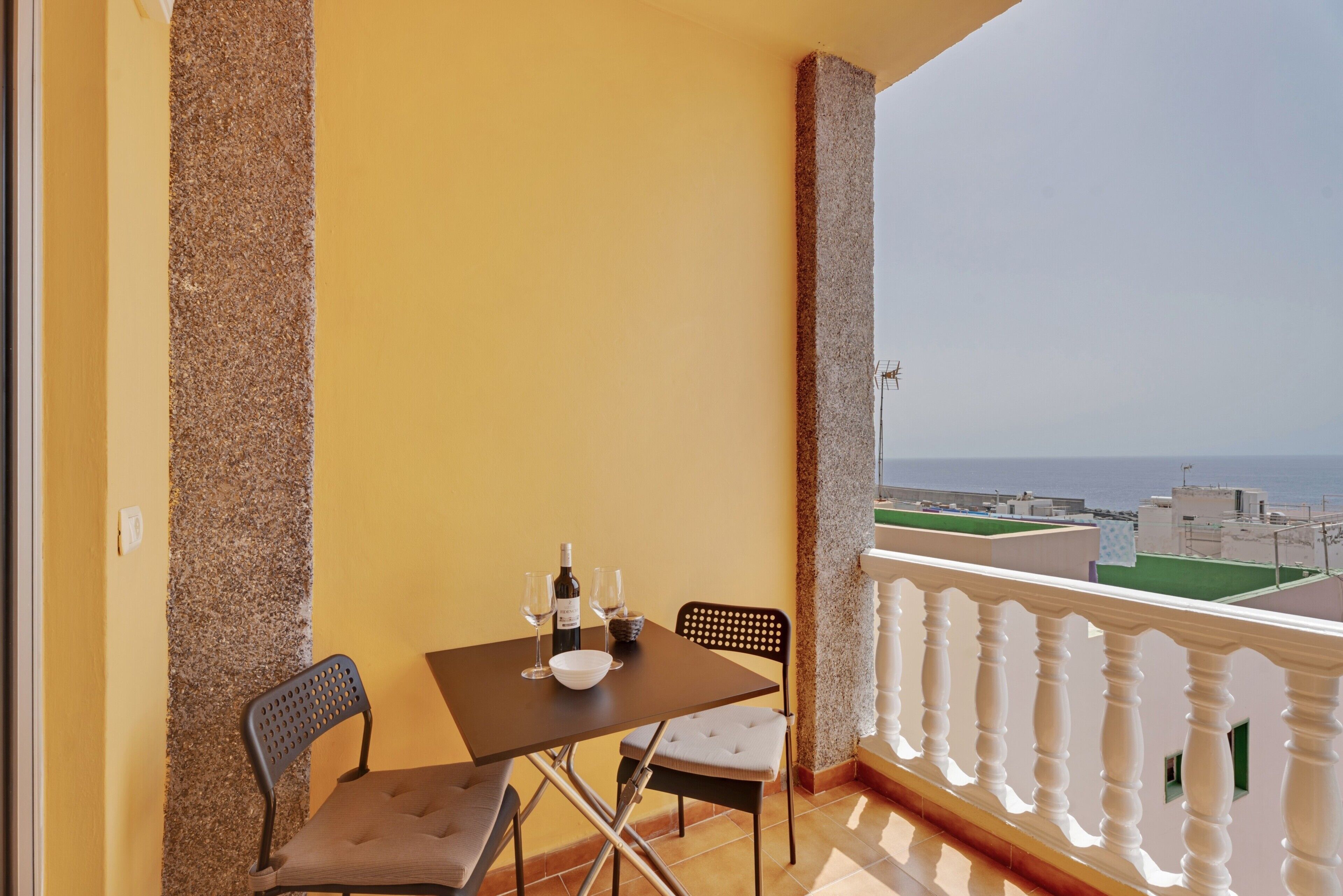 A balcony with a table, chairs, and a view of the sea.