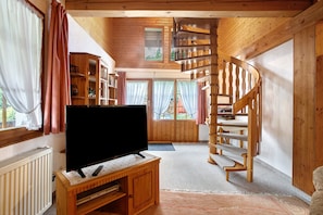 Un intérieur en bois avec un téléviseur posé sur un meuble en bois, un escalier en colimaçon et une fenêtre avec des rideaux.