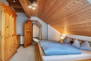 Une chambre avec un plafond en pente, une armoire en bois et un lit avec une literie à rayures.