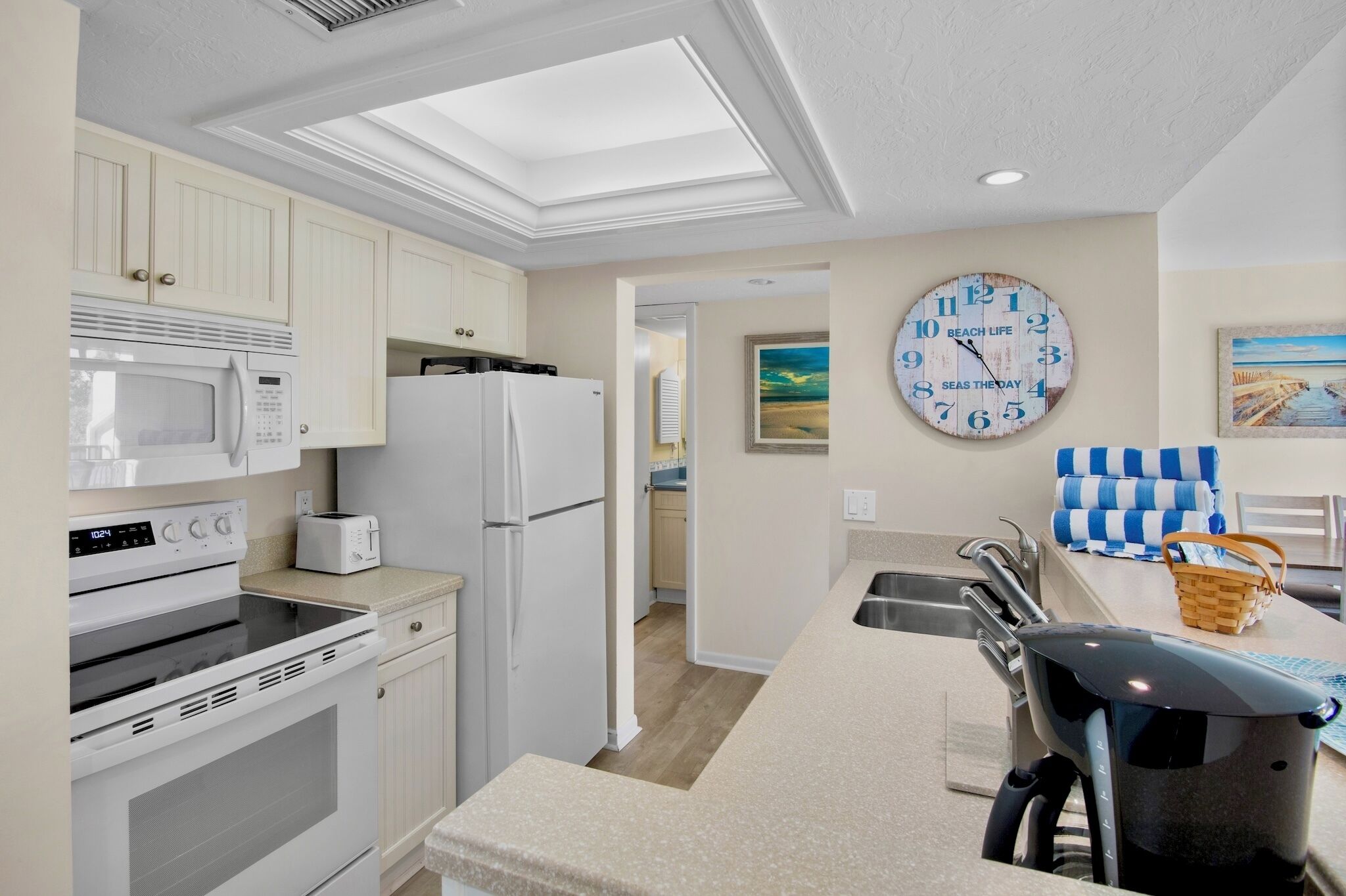 A kitchen with white cabinets, a microwave, a refrigerator, a toaster, and a clock on the wall.