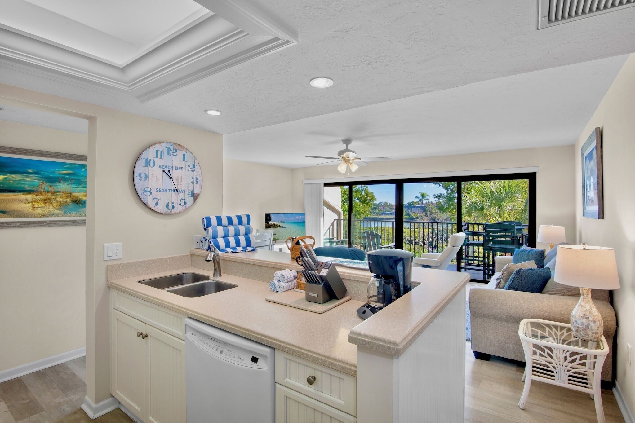A modern kitchen with a central island, a dining area with a view, and a living room with a sofa and a lamp.
