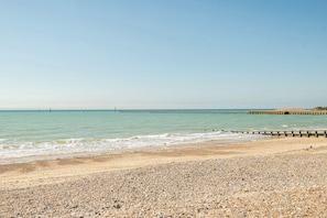 Une plage de galets avec une jetée en bois qui s’avance dans la mer.