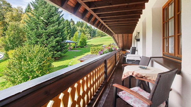A balcony with a wooden railing, a table with chairs, and a view of a green landscape with trees and a grassy area. - Apartment 3 with Shared Garden, Balcony and Wi-Fi (Todtmoos)