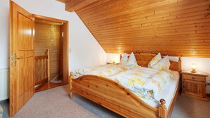 A bedroom with a wooden ceiling, a bed with floral bedding, a nightstand with a lamp, and a wooden door leading to another room. - Apartment 3 with Shared Garden, Balcony and Wi-Fi (Todtmoos)