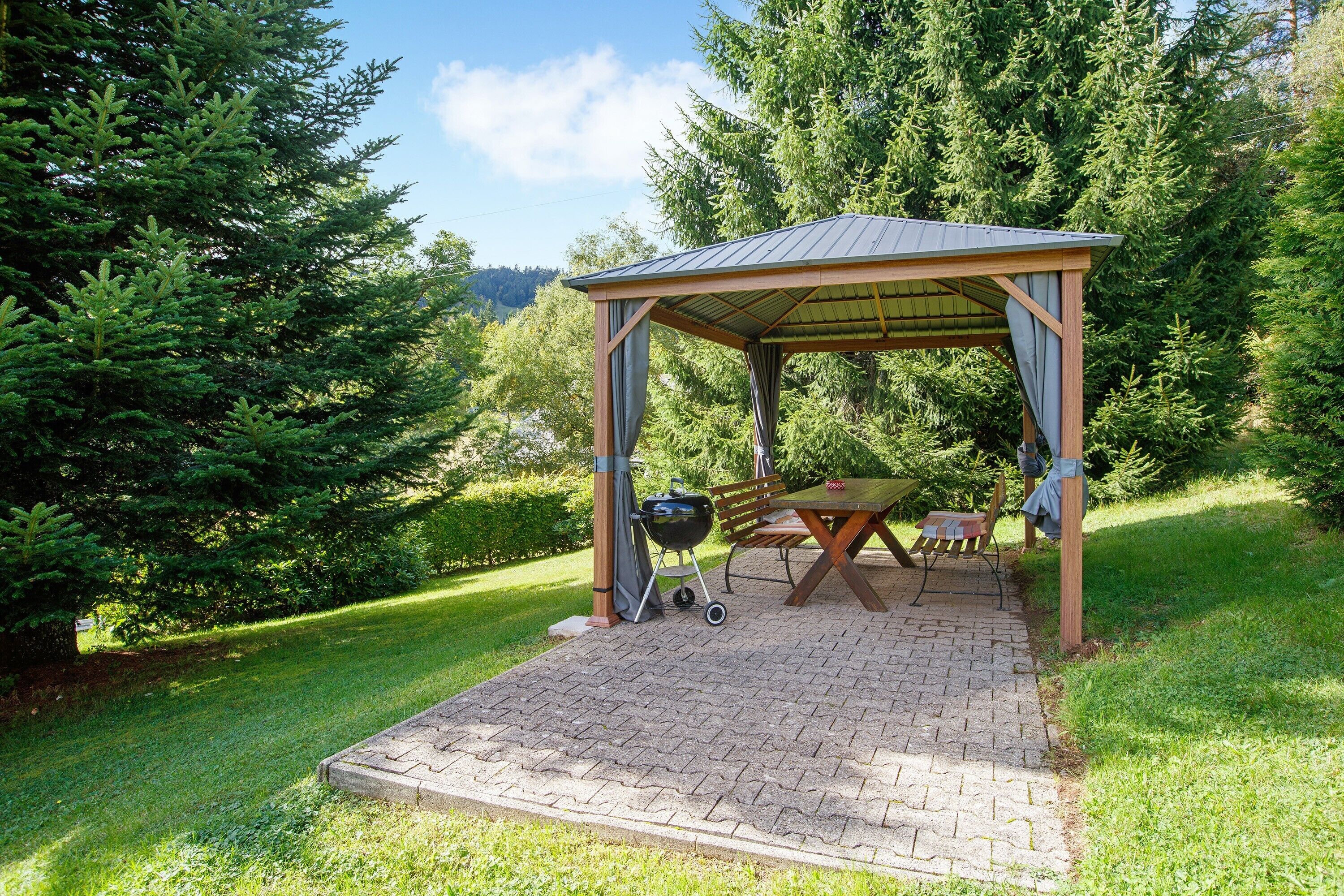 Een overdekt terras met een tafel, stoelen, een barbecue en een geplaveid pad.