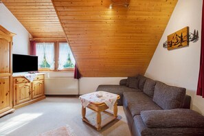 Et hyggeligt værelse med trælofter, en sofa, et lille bord, et fjernsyn og et vindue med gardiner.