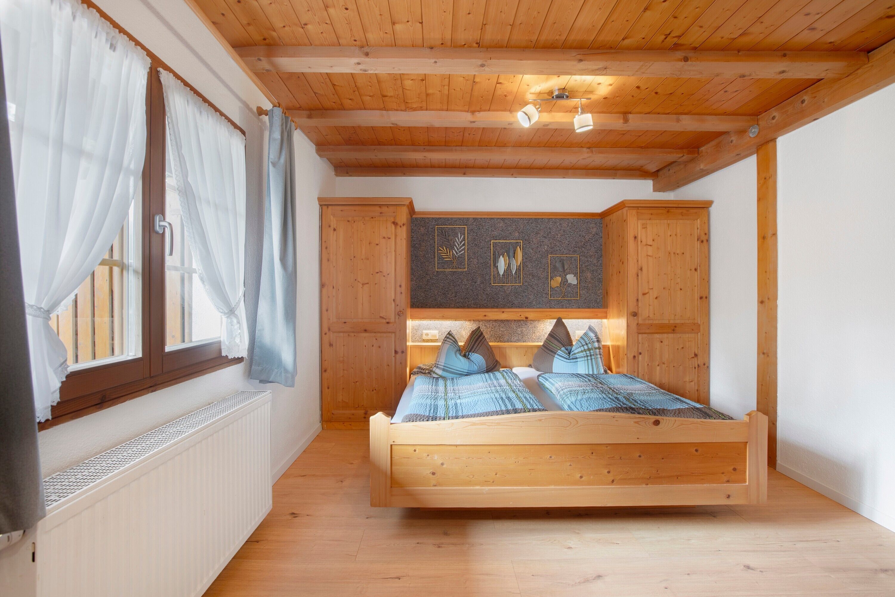 Ein schlicht eingerichtetes Schlafzimmer mit Holzbett, Heizkörper und Bildern an der Wand.