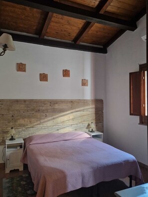 Un dormitorio con cabecera de madera, cama con edredón rosa, dos mesitas de noche con lámparas y tres adornos colgados en la pared.
