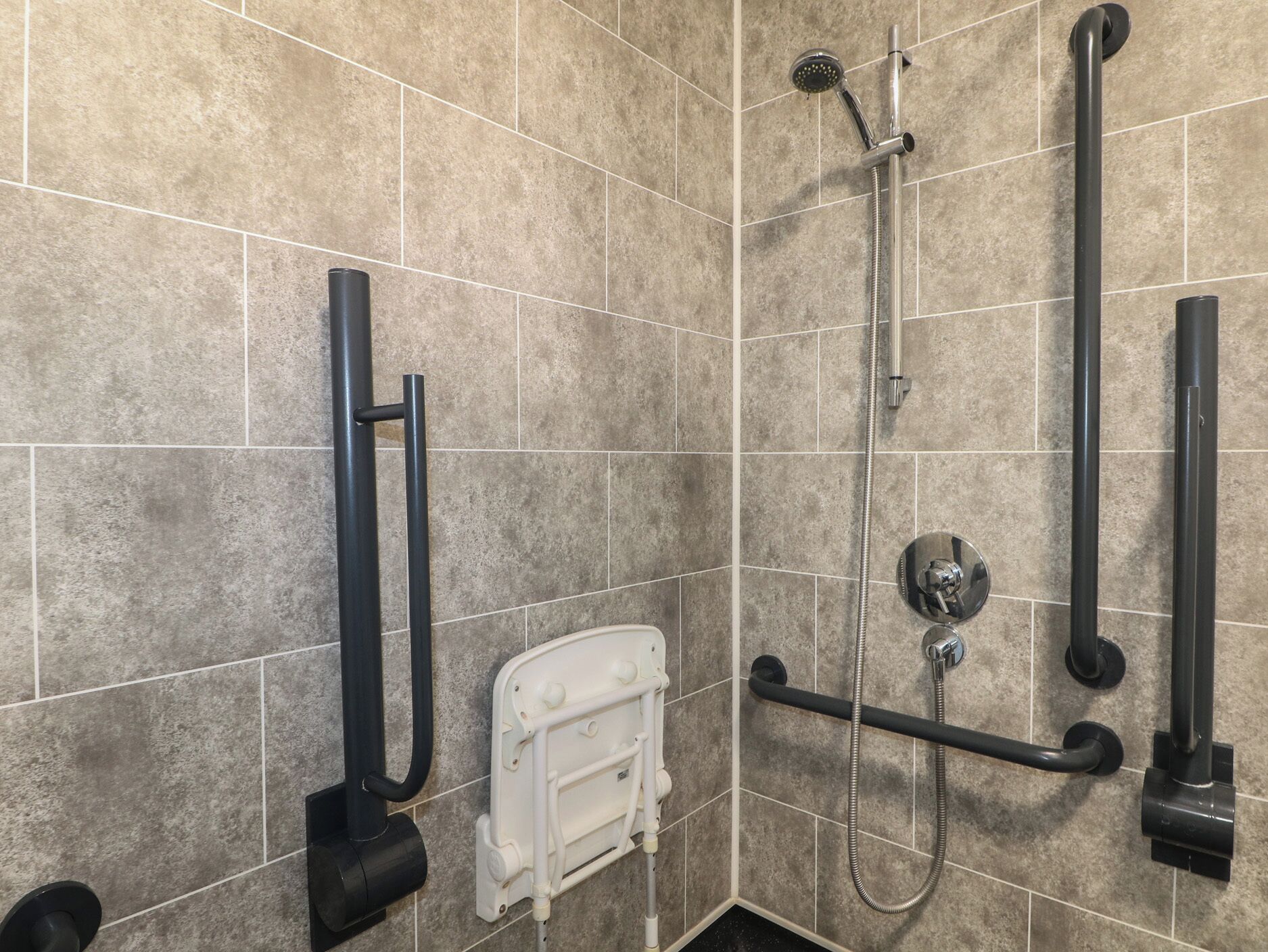 Une salle de bain équipée d’une douche, de barres d’appui et d’un sèche-mains blanc.