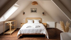 A bedroom with a sloped ceiling, a bed with white linens, a wooden bedside table, a hanging light fixture, and a radiator. - Bali apartment with patio - Le Mans, apartment with patio - Le Mans (Le Mans)