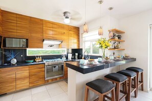 Eine moderne Küche mit Holzausstattung, einer zentralen Kochinsel mit Hockern, einem eingebauten Backofen und einer Mikrowelle.