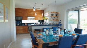 Une cuisine moderne avec des meubles en bois, un coin repas avec des chaises bleues et une grande fenêtre qui laisse entrer la lumière naturelle.